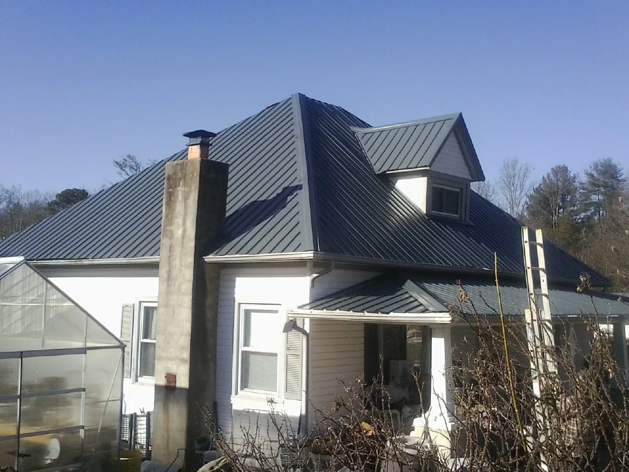 Dark blue standing seam metal roof on a white farmhouse with dormer — Slate & Tile Roof Repair by Roofing Brothers in Horseshoe Bend