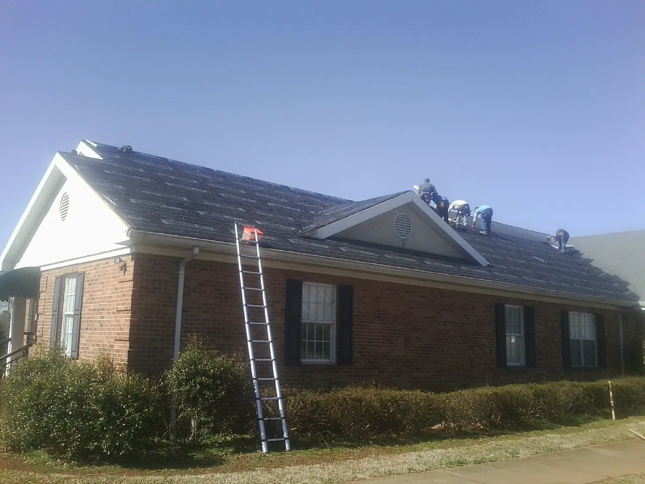 Crew tearing shingles off a brick ranch roof with a ladder set — Metal Roof Repair work by our crew in Horseshoe Bend