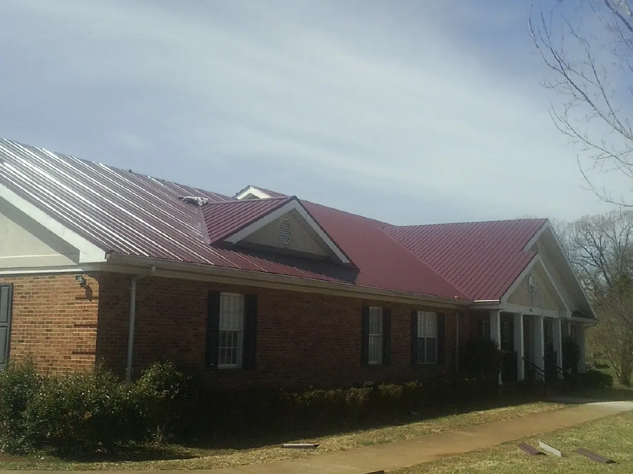 Red metal roof with gabled entries on a long brick building, from a Hail Damage Roof Repair job in Horseshoe Bend