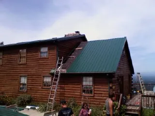 Green metal roof going on a two story log home with ladders set in Horseshoe Bend