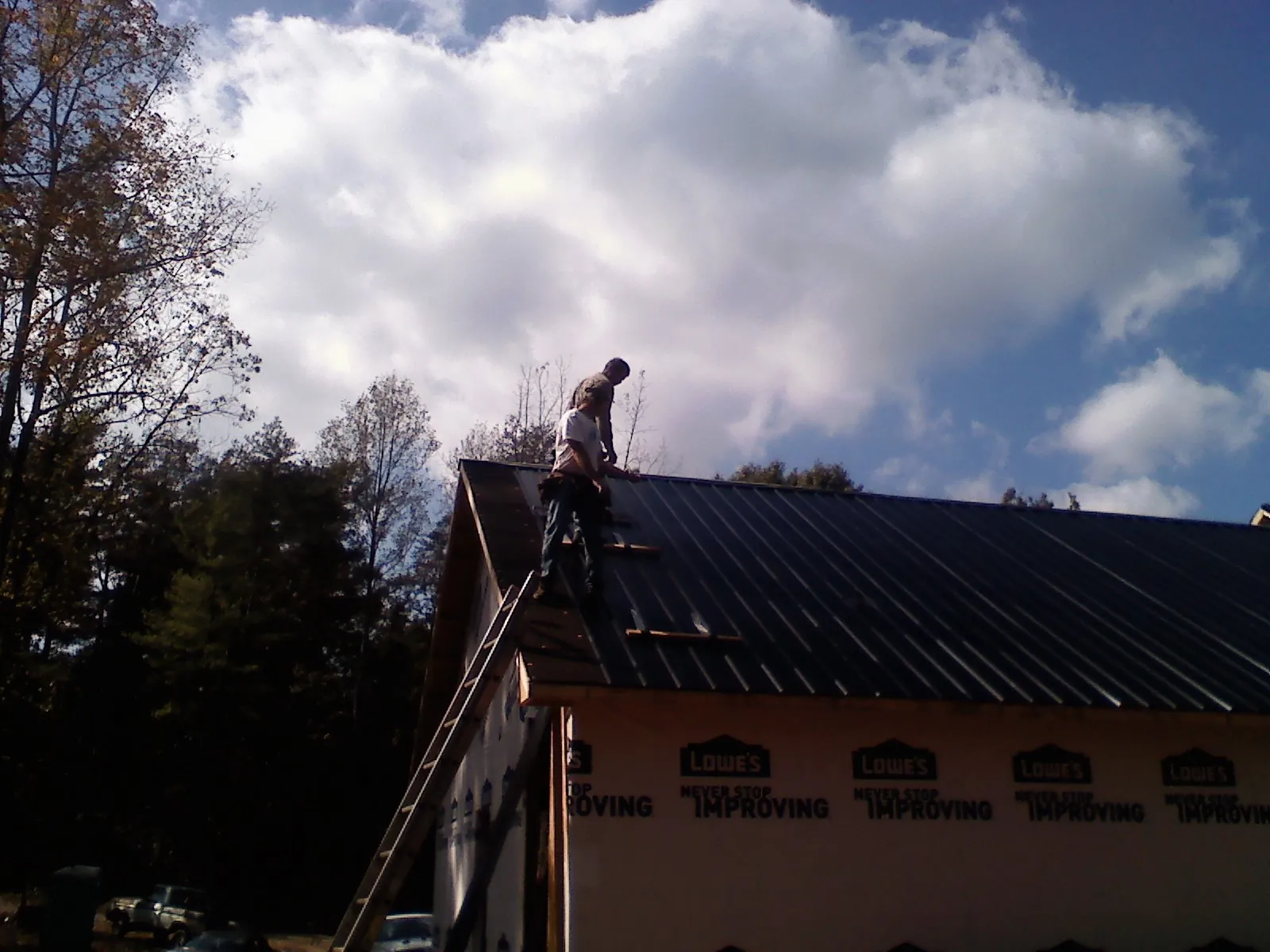 Roofer fastening dark metal panels high against a cloudy sky, from a Roof Inspection job in Horseshoe Bend