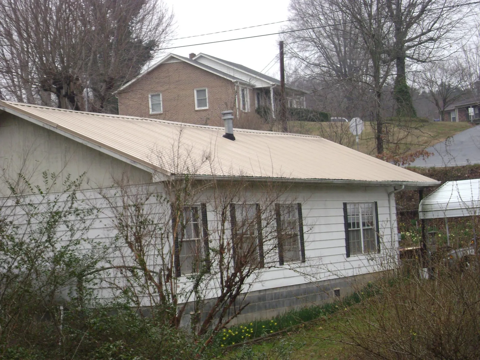 Tan metal roof on a white sided house set into a hillside — Commercial Roofing by Roofing Brothers in Horseshoe Bend