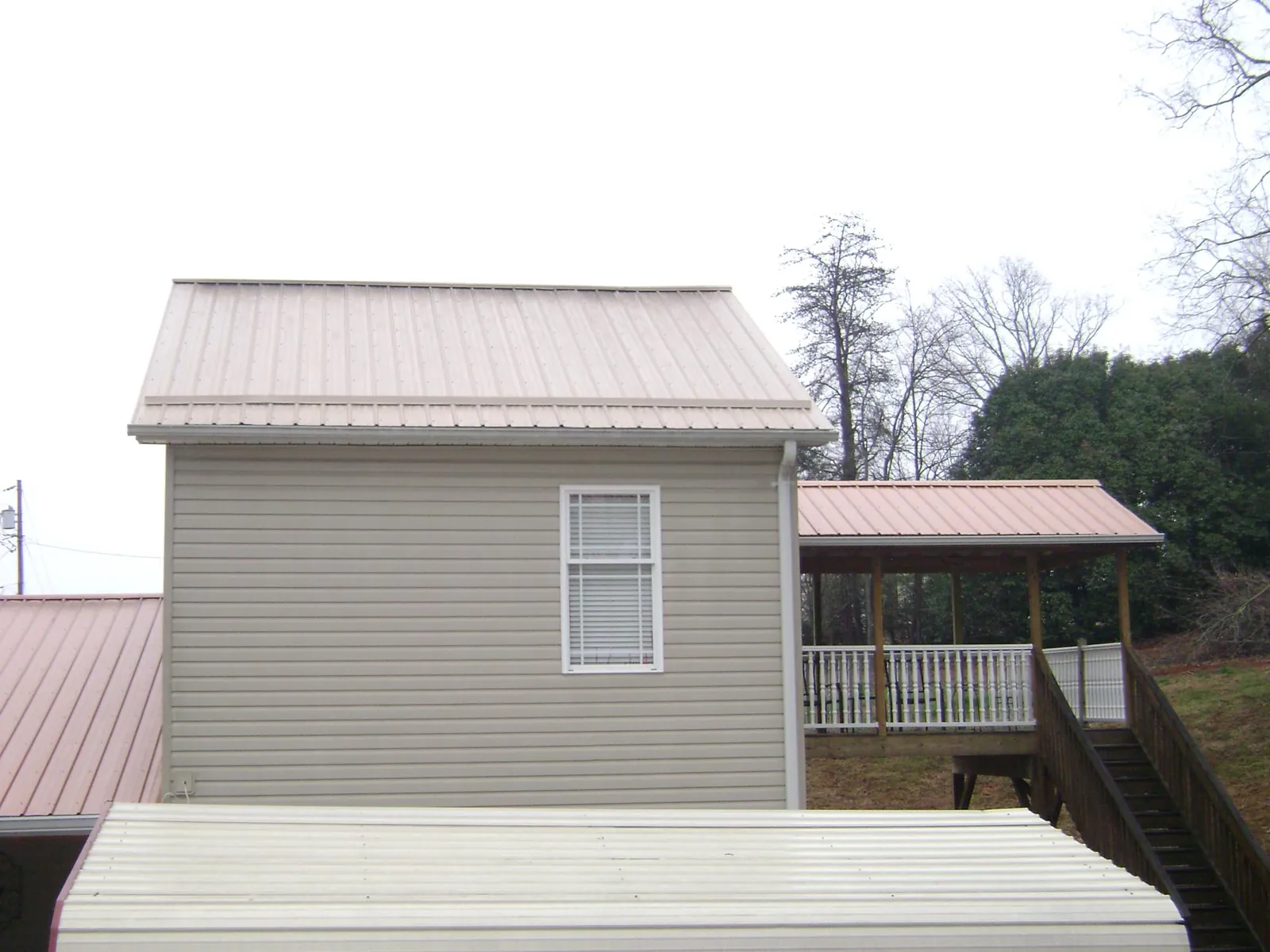 Tan metal roofs on a two story addition and attached porch, from a Roof Replacement job in Horseshoe Bend